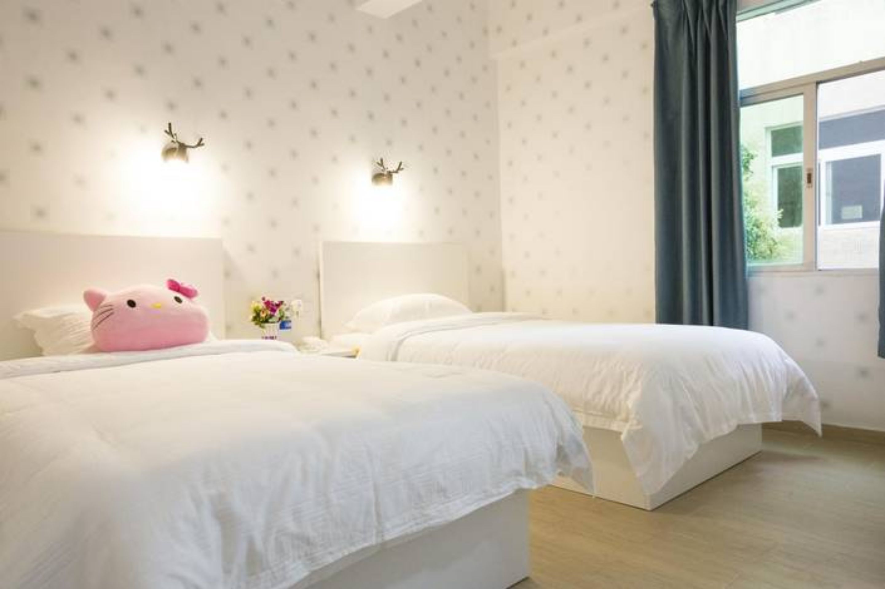 Habitación de hotel con dos camas, una ventana con cortinas e iluminación en la pared.
