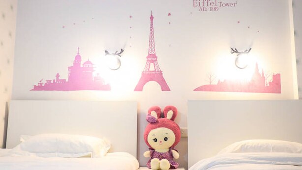 A hotel room with a bed, a nightstand, and a wall decoration featuring the Eiffel Tower and a plush toy. - Jiulongwan Boutique Apartment (Zhuhai)