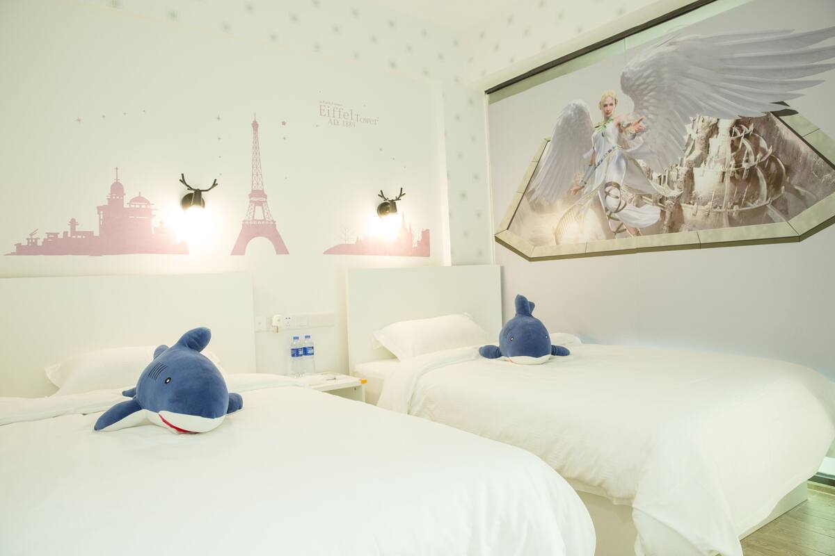 A hotel room with two beds, a wall mural of the Eiffel Tower, and a framed picture of an angel.