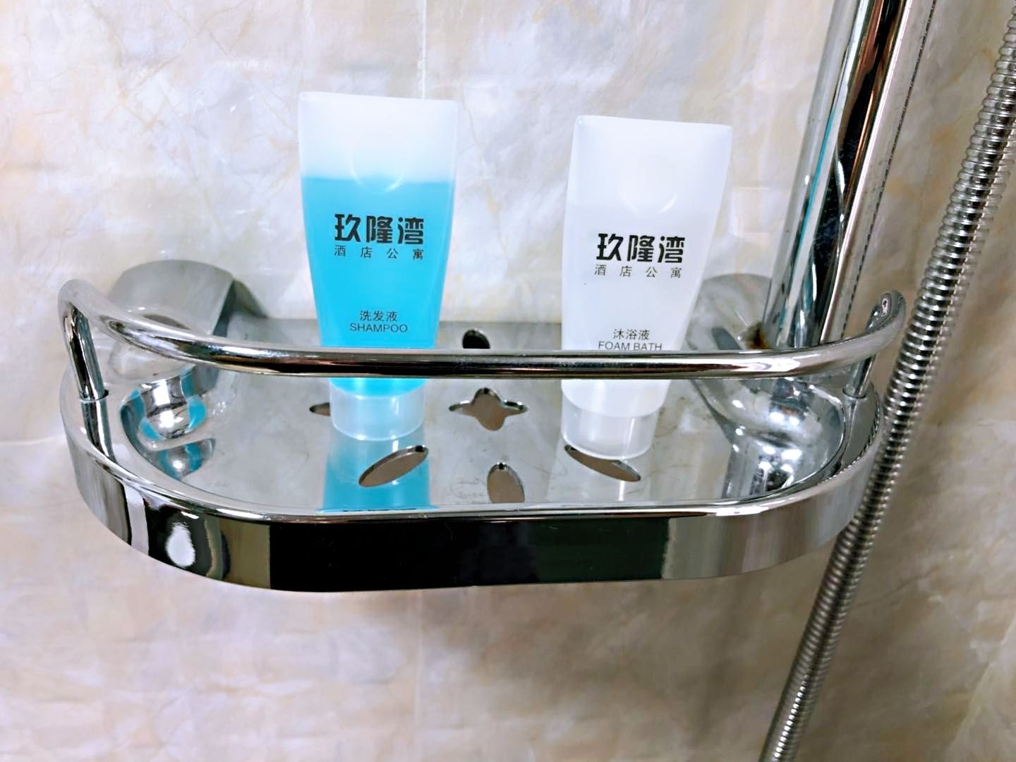 A shower area with a chrome shower tray holding two bottles of shampoo and a bottle of foam bath.