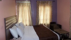 A bedroom with a bed, a bedside table, and curtains. - A2 Suites (Lagos)