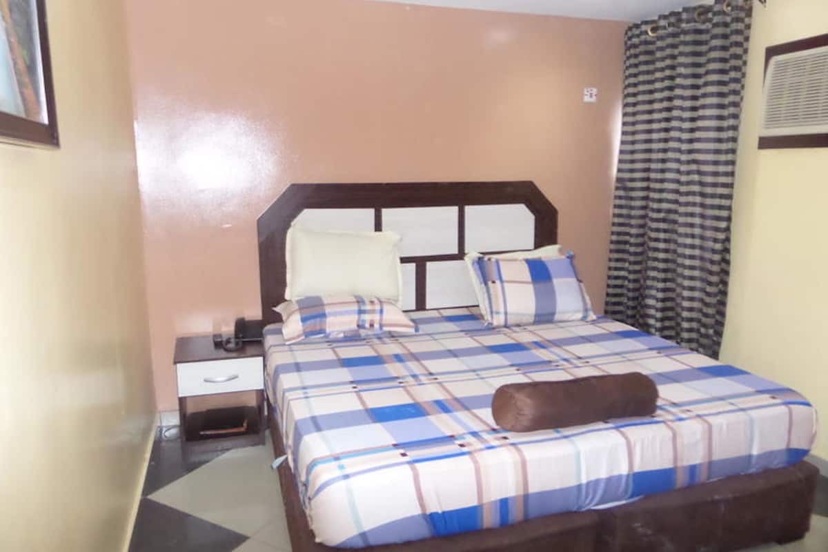 A bedroom with a bed, a nightstand, a lamp, and a window with curtains.