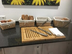 A kitchen counter with baskets of bread and a cutting board with a knife and a book. - Hotel an der Burgschänke (Alpen)