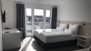 Ein Hotelzimmer mit einem Bett, einem Schreibtisch, einem Stuhl, einem kleinen Tisch und Blick ins Freie durch das Fenster.