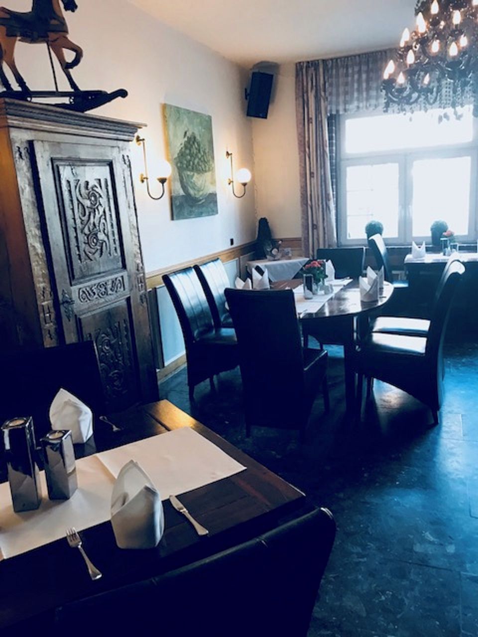 A dining area with tables, chairs, a chandelier, and a decorative cabinet.