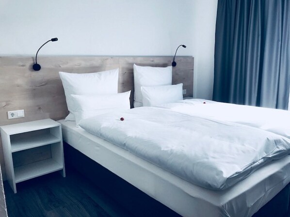 A double bed with white linens, a wooden headboard, bedside tables, and a nightstand. - Hotel an der Burgschänke (Alpen)