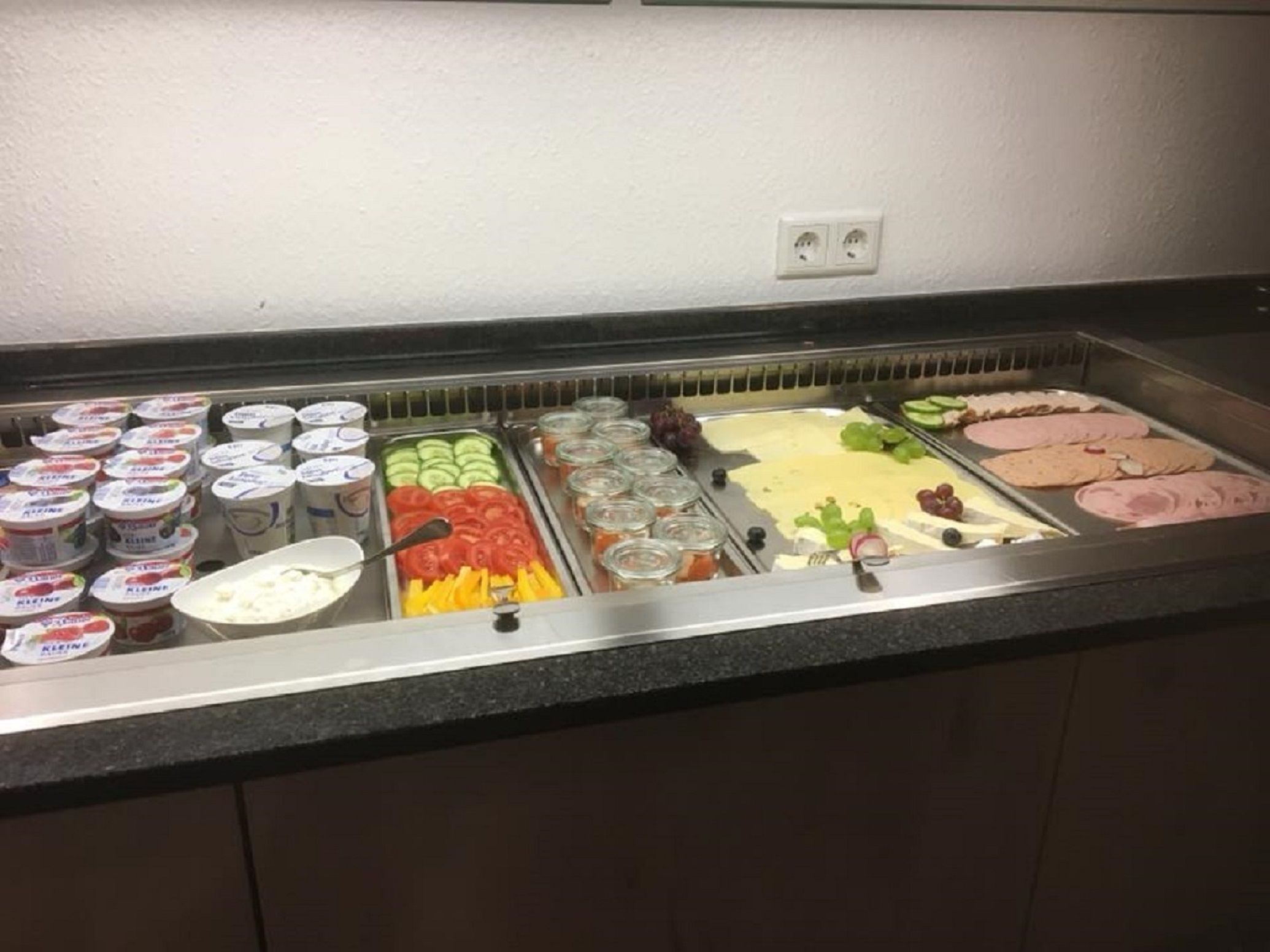 Un bufé con diversas opciones de comida, incluyendo yogur, verduras y carnes.