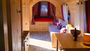 A cozy, wooden interior with a bed, seating area, and a table with a bottle. - Gîte Amboise - Roulotte Chais Catherine (Amboise)