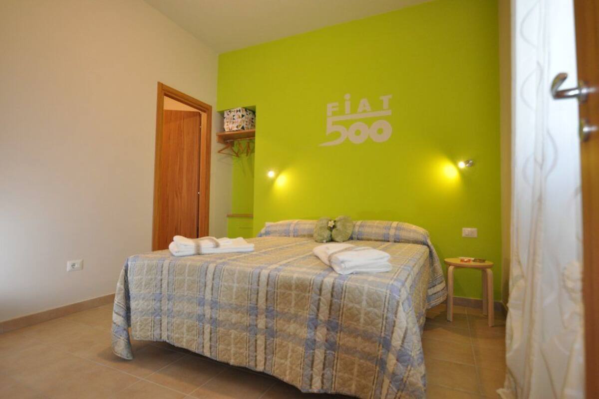 A hotel room with a bed, a green wall, and a FIAT 500 logo.
