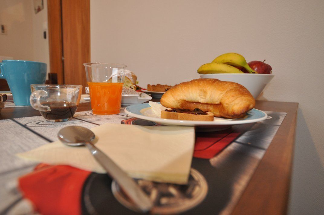 Une table dressée pour le petit-déjeuner avec un sandwich au croissant, un bol de fruits, un verre de jus d’orange et une tasse de café.