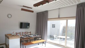 Une cuisine moderne avec un plan de travail en bois, une table à manger avec des chaises, un téléviseur fixé au mur et une grande porte-fenêtre coulissante donnant sur un patio extérieur.