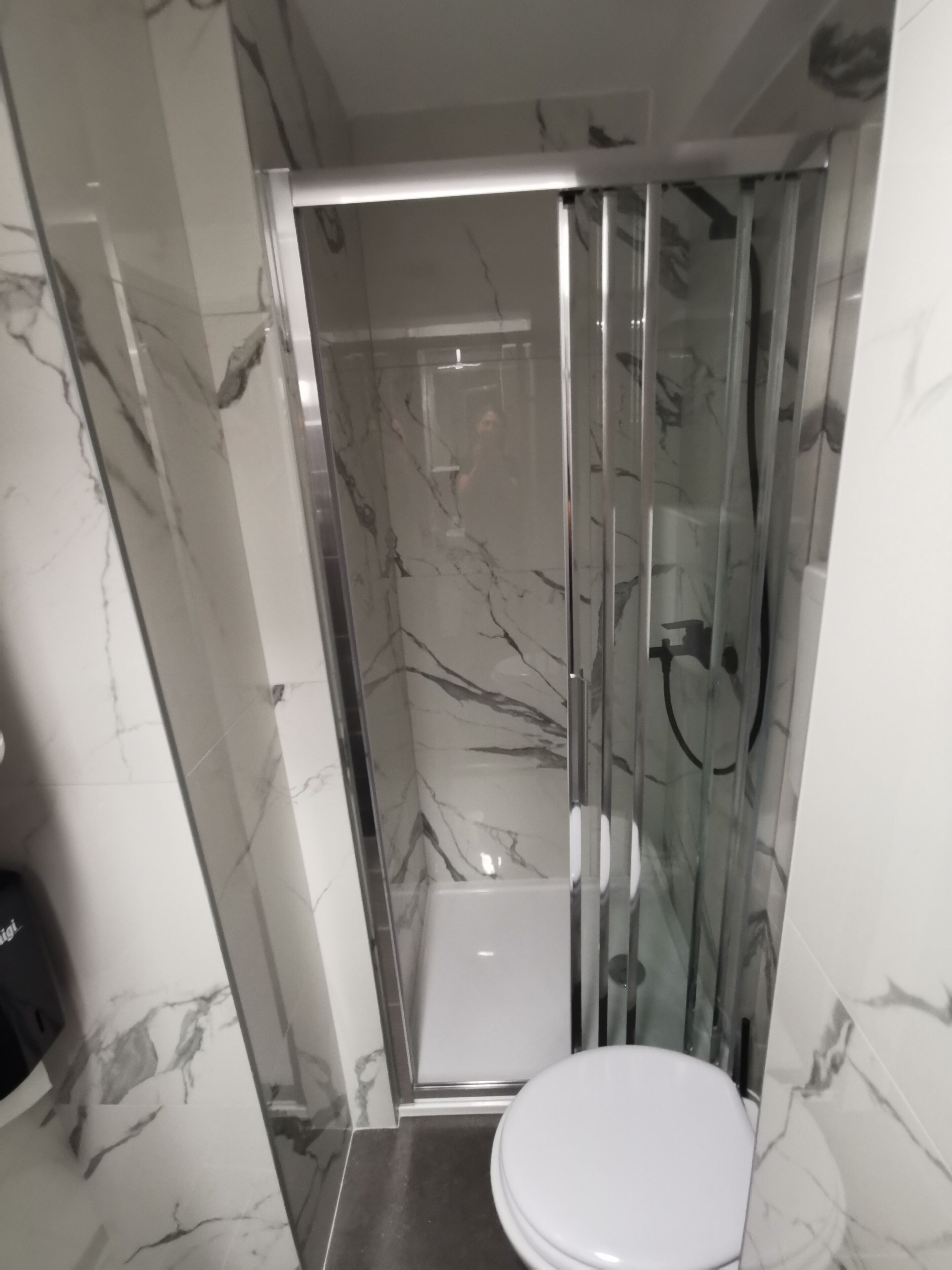 A bathroom with a glass-enclosed shower, a white toilet, and marble-patterned walls.