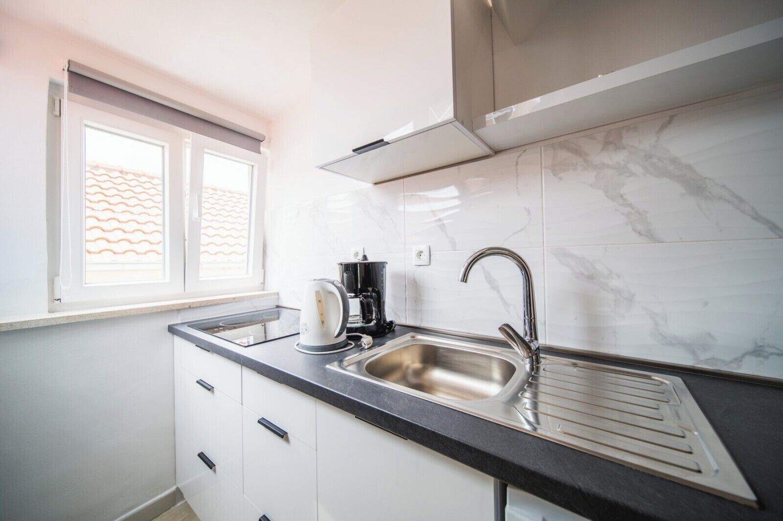 A modern kitchen with a stainless steel sink, a coffee maker, and a window with blinds.