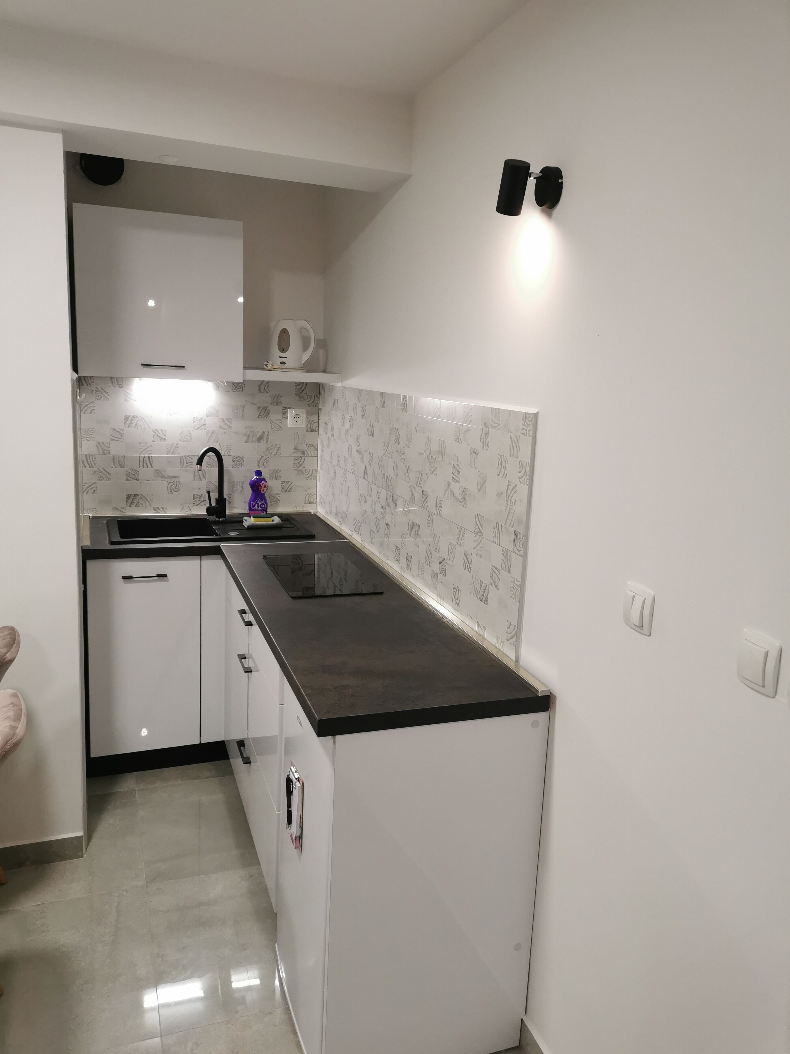 A compact kitchen with white cabinets, a black countertop, and patterned backsplash tiles.