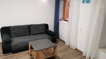 Una habitación con un sofá gris, una mesa de centro de madera y una ventana con vistas a barcos.