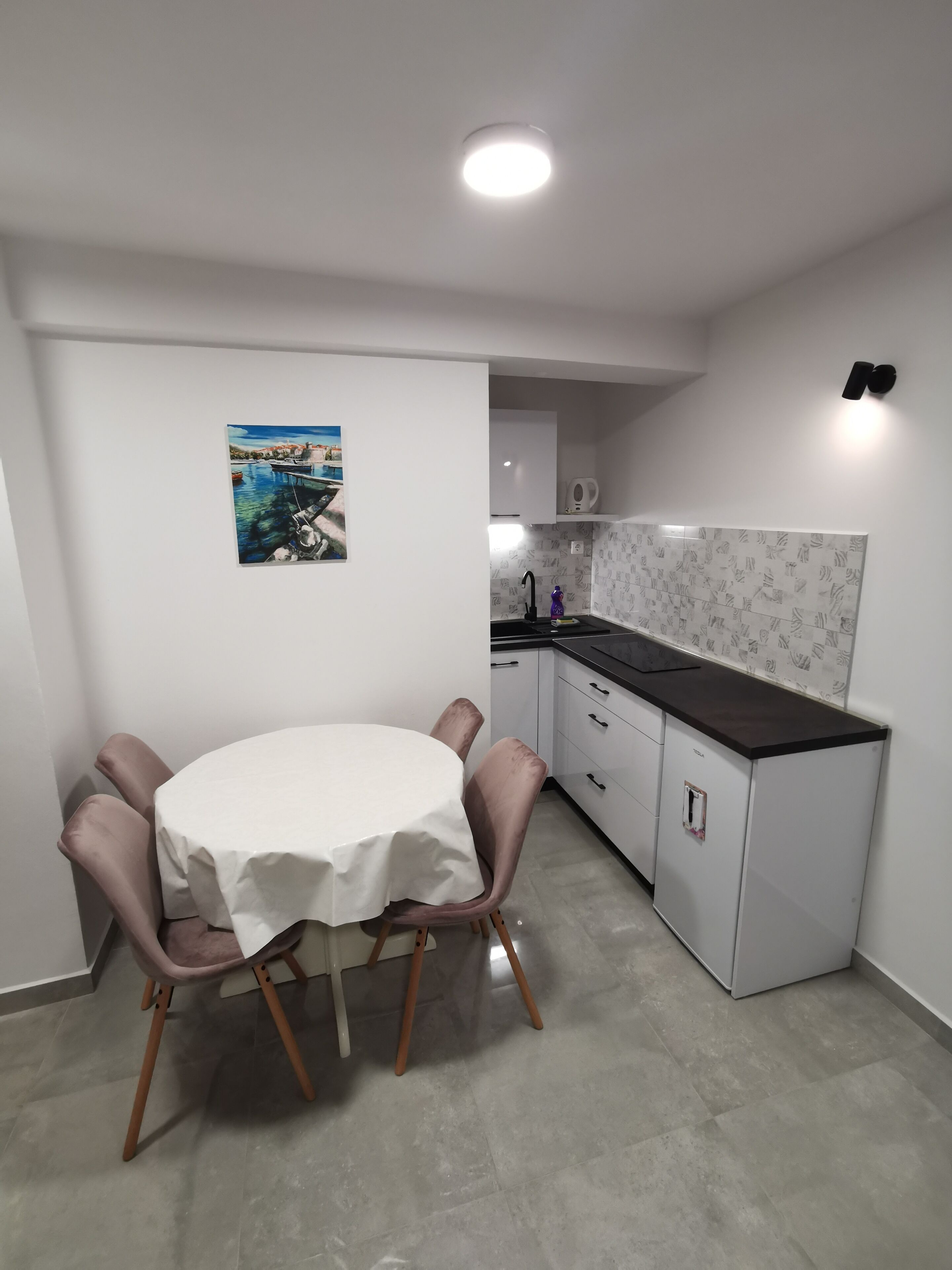 Una cucina compatta con zona pranzo, caratterizzata da un tavolo bianco con tovaglia bianca, una sedia viola e una piccola isola con lavandino.