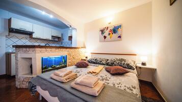 A bedroom with a stone fireplace, a bed with towels, a world map on the wall, and a kitchen area with cabinets and a stove.