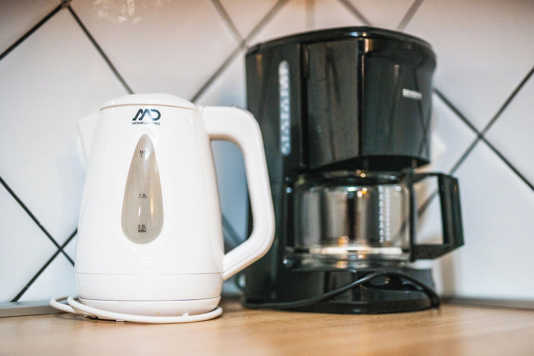 En vit vattenkokare och en svart kaffebryggare står på en köksbänk.