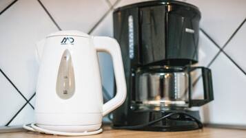 En vit vattenkokare och en svart kaffebryggare står på en köksbänk.