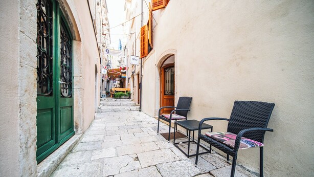 A narrow alleyway with stone pavement, two wicker chairs, and a green door. - M & J Central Suites (Korcula)