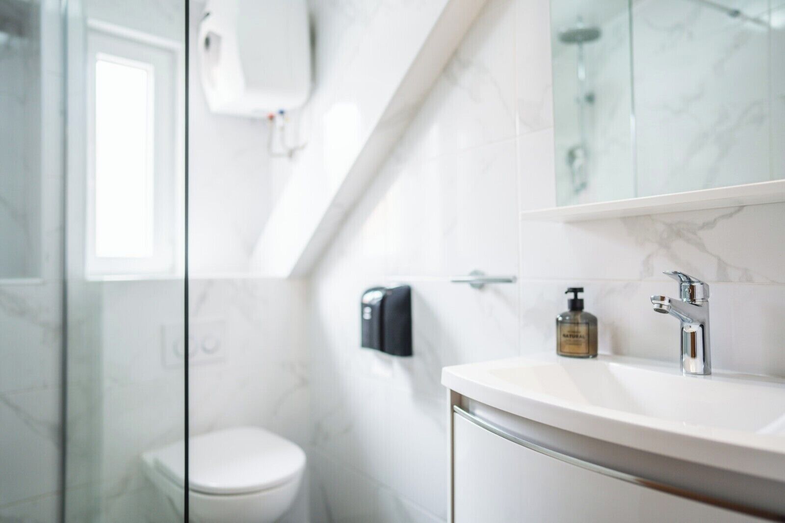 Ein modernes Badezimmer mit Duschkabine aus Glas, einer weißen Toilette und einem Waschtisch mit chromfarbenem Wasserhahn und Seifenspender.