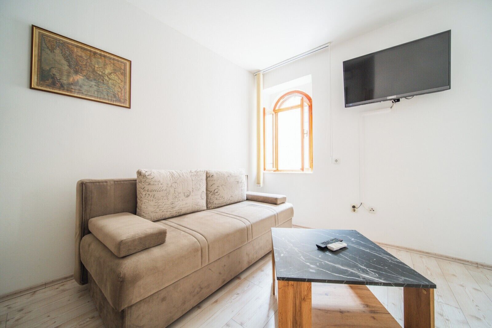 Un salón minimalista con un sofá color beige, una mesa de centro de madera, un televisor de pantalla plana y un mapa enmarcado en la pared.