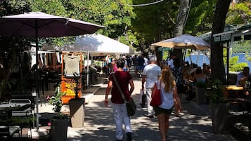Une rue piétonne bordée de cafés et de boutiques en plein air, ombragée par des arbres, où l’on peut voir des gens se promener et prendre leurs repas.