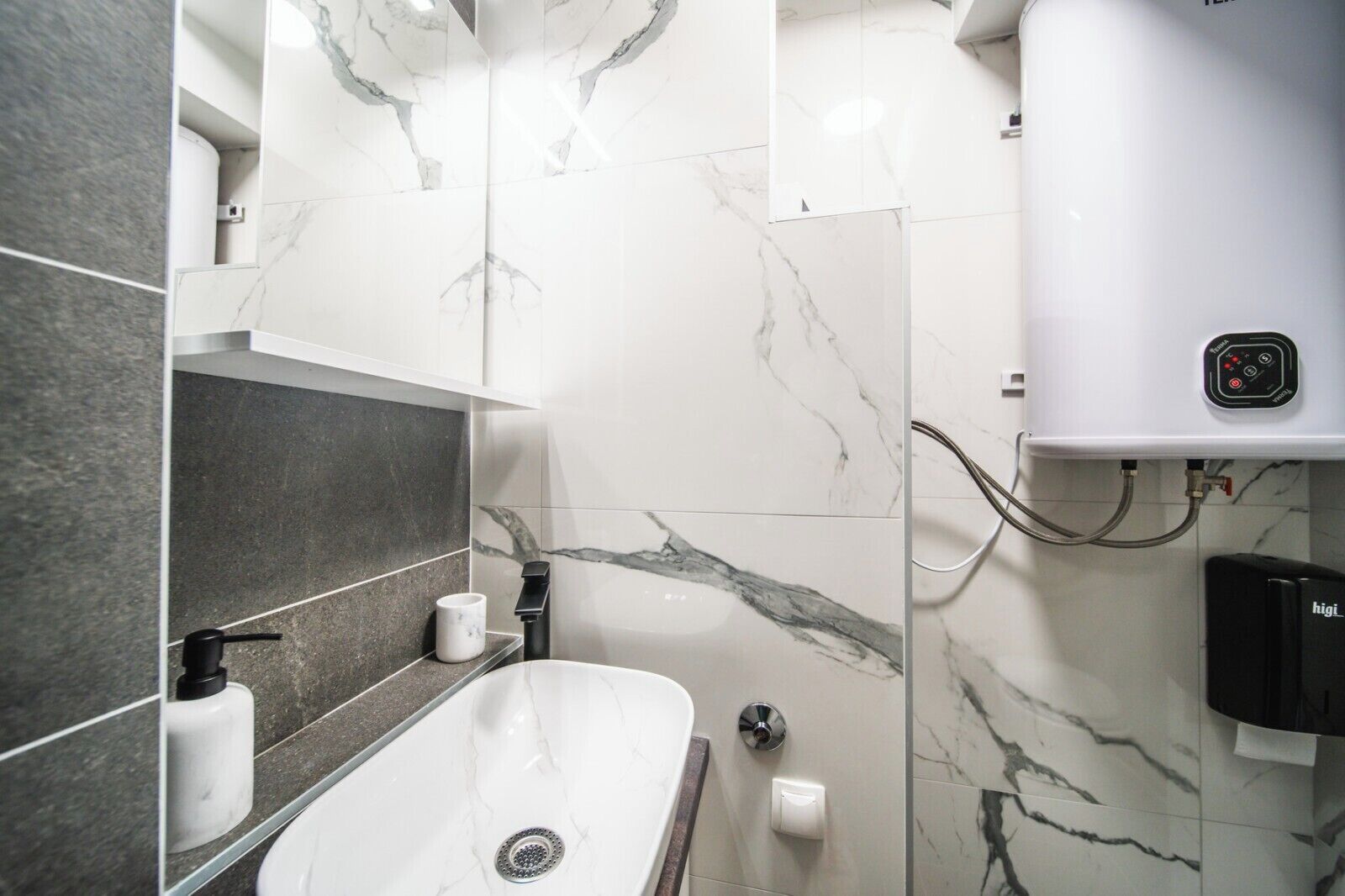 Une salle de bain moderne avec un lavabo blanc, des murs en marbre et un chauffe-eau.