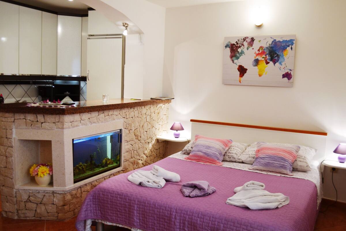 A hotel room with a stone fireplace, a bed with towels, a world map on the wall, and a small fish tank.