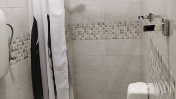 Een kleine douchecel met betegelde wanden, een witte douchegordijn, een handdouche en een wit toilet.
