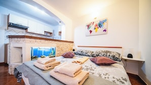 A bedroom with a bed, towels, pillows, a nightstand, a lamp, a map on the wall, and a stone fireplace. - M & J Central Suites (Korcula)