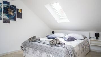 A bedroom with a sloped ceiling, a skylight, a bed with a grey and white patterned bedspread, and three framed pictures on the wall.