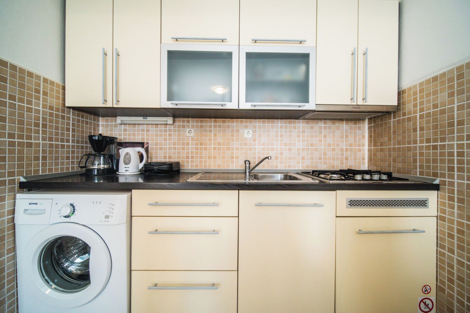 A compact kitchen with a washing machine, a coffee maker, and a stove.