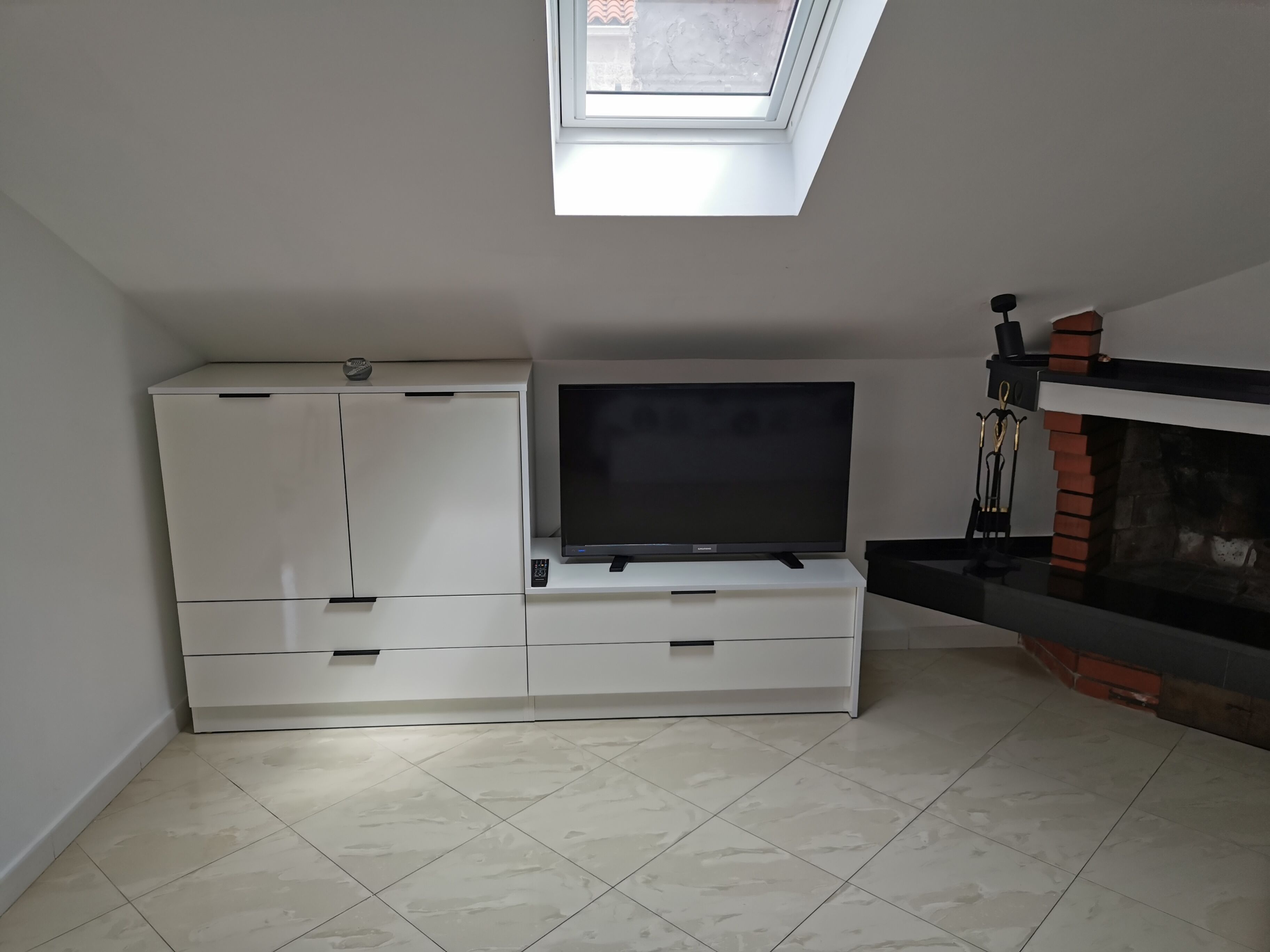 Una sala de estar moderna con un televisor de pantalla plana sobre un mueble blanco, una chimenea y un tragaluz.
