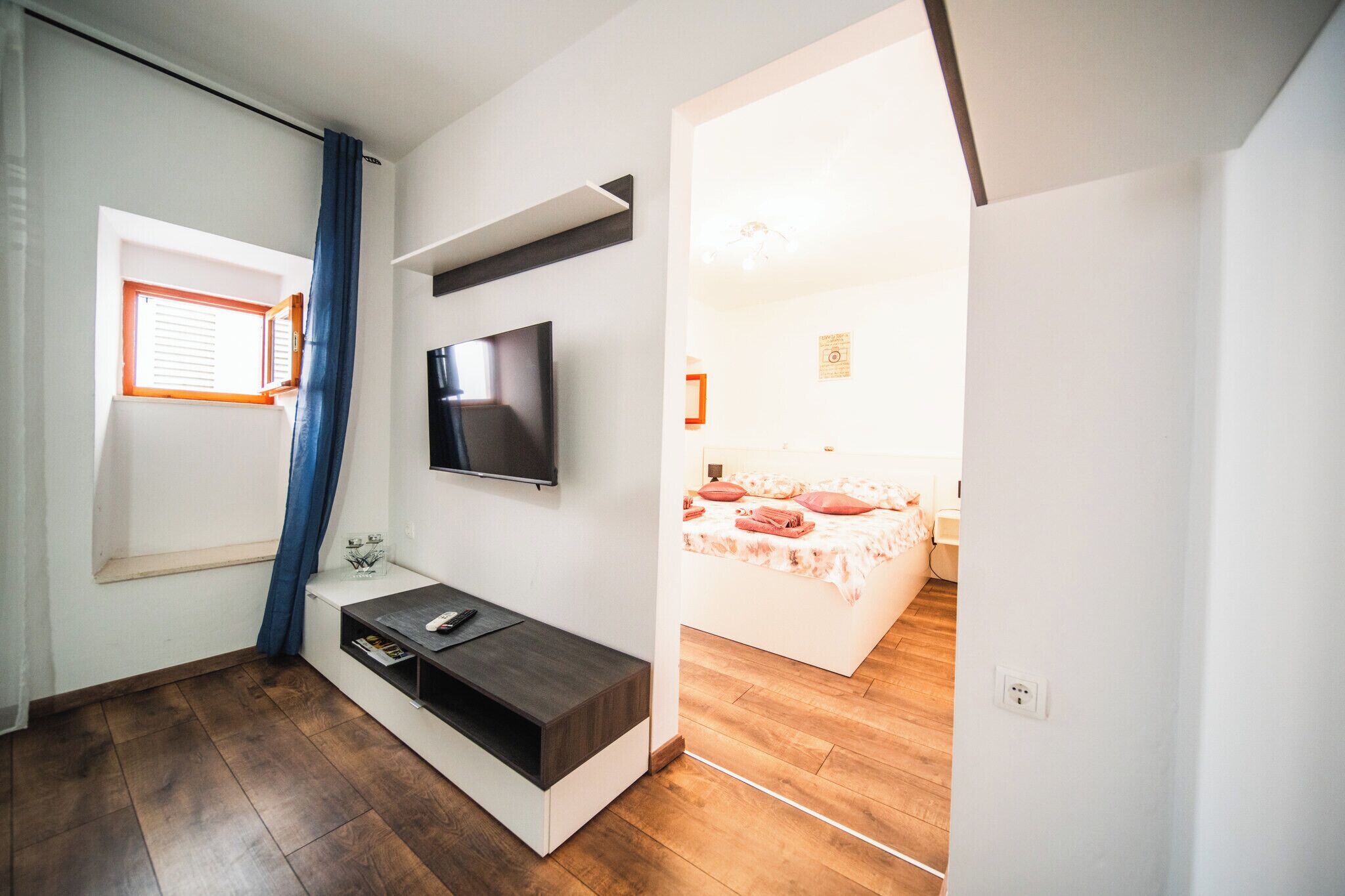 A modern bedroom with a TV mounted on the wall, a window with curtains, a bedside table, and a bed with a floral bedspread.