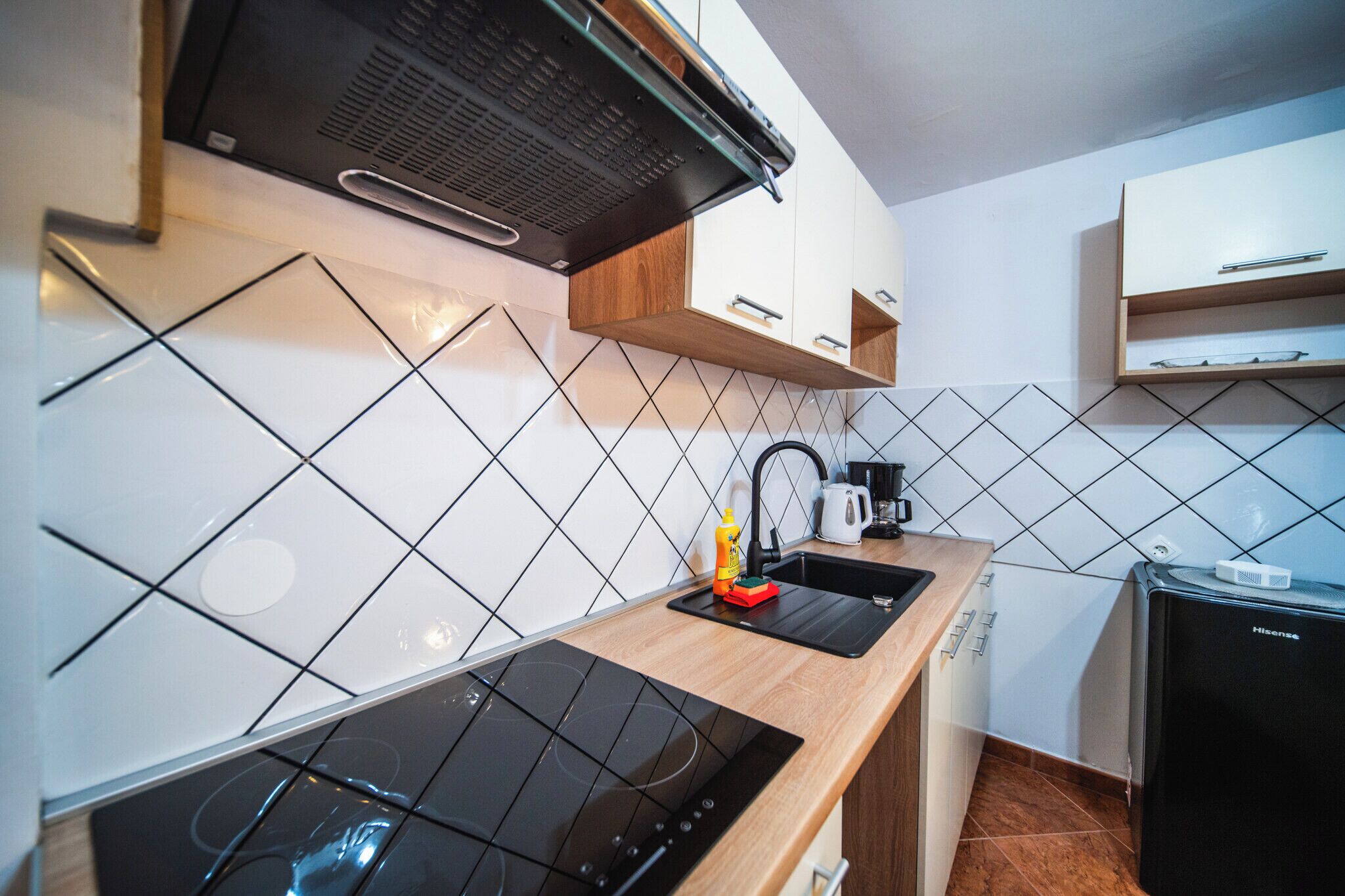 Uma cozinha moderna com um fogão por indução preto, forno embutido, cafeteira e geladeira compacta.