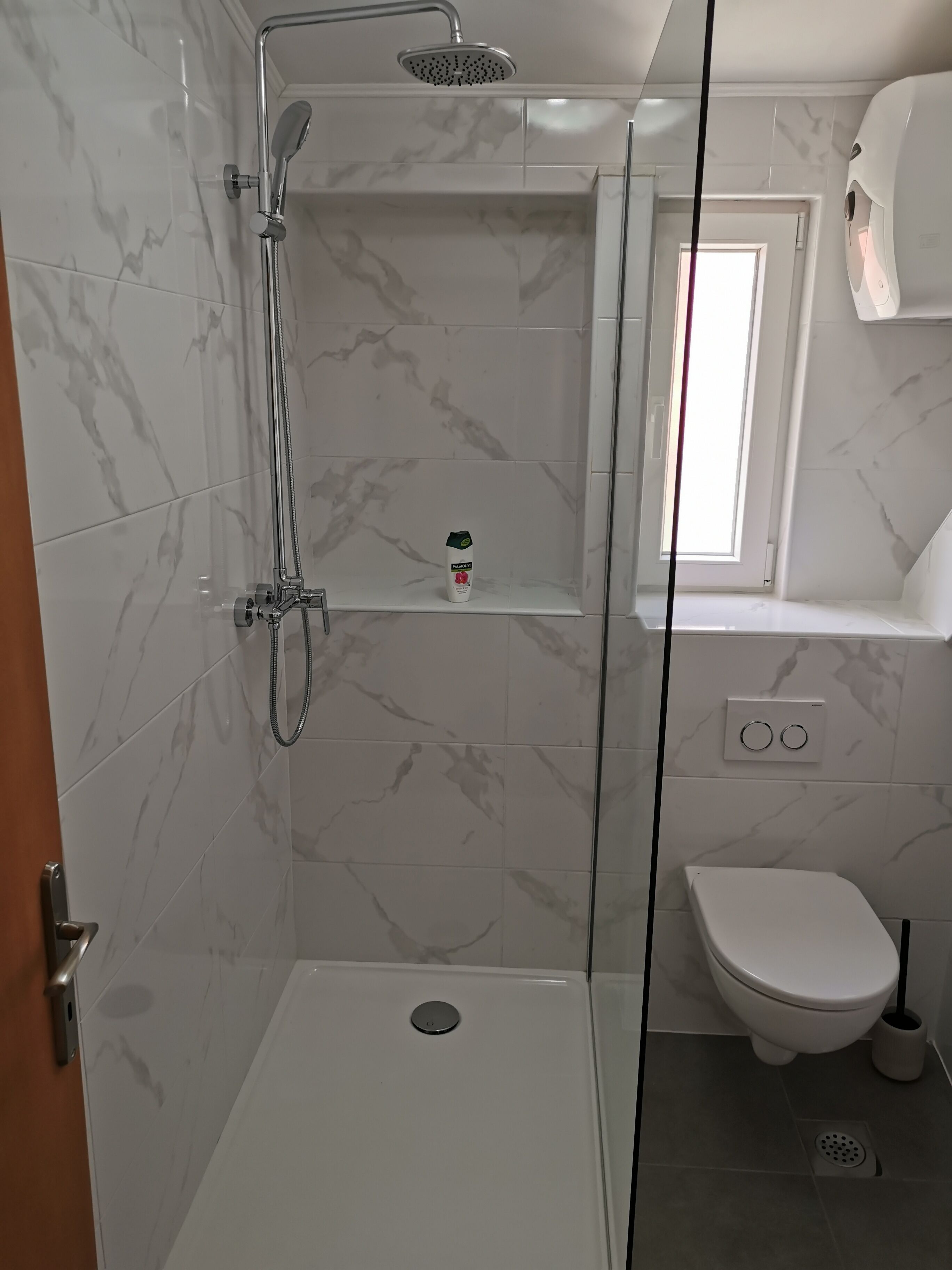 A bathroom with a glass-enclosed shower, a toilet, and a small window.
