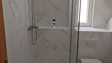 A bathroom with a glass-enclosed shower, a toilet, and a small window.
