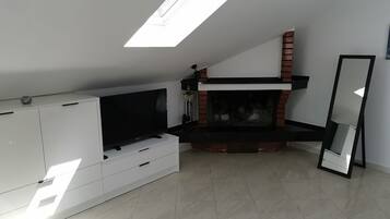 Un salon moderne doté d’un téléviseur à écran plat, de meubles blancs, d’une cheminée et d’une lucarne.