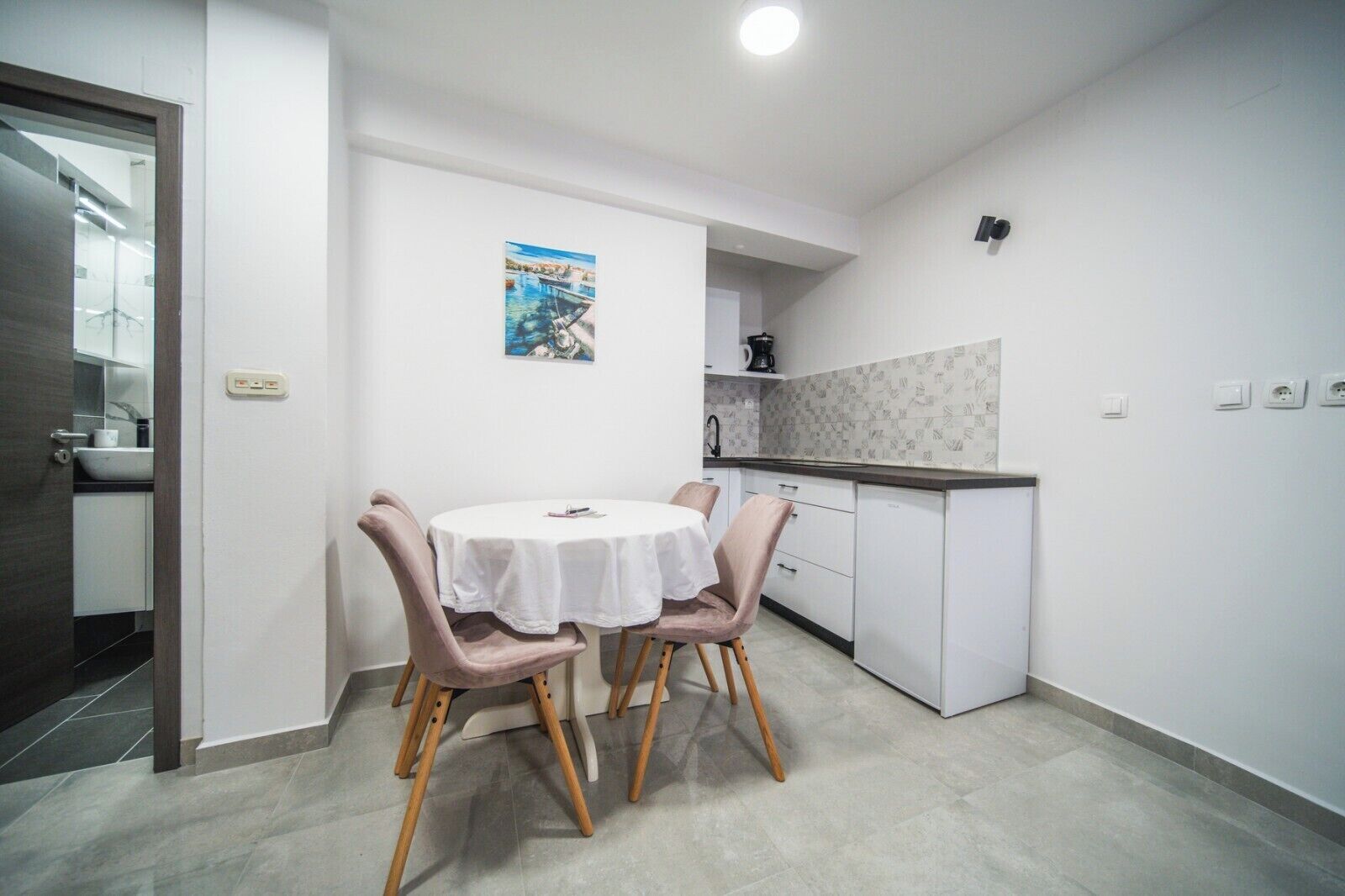 A compact kitchen with a dining area, featuring a round table with chairs, a small island, and a poster on the wall.