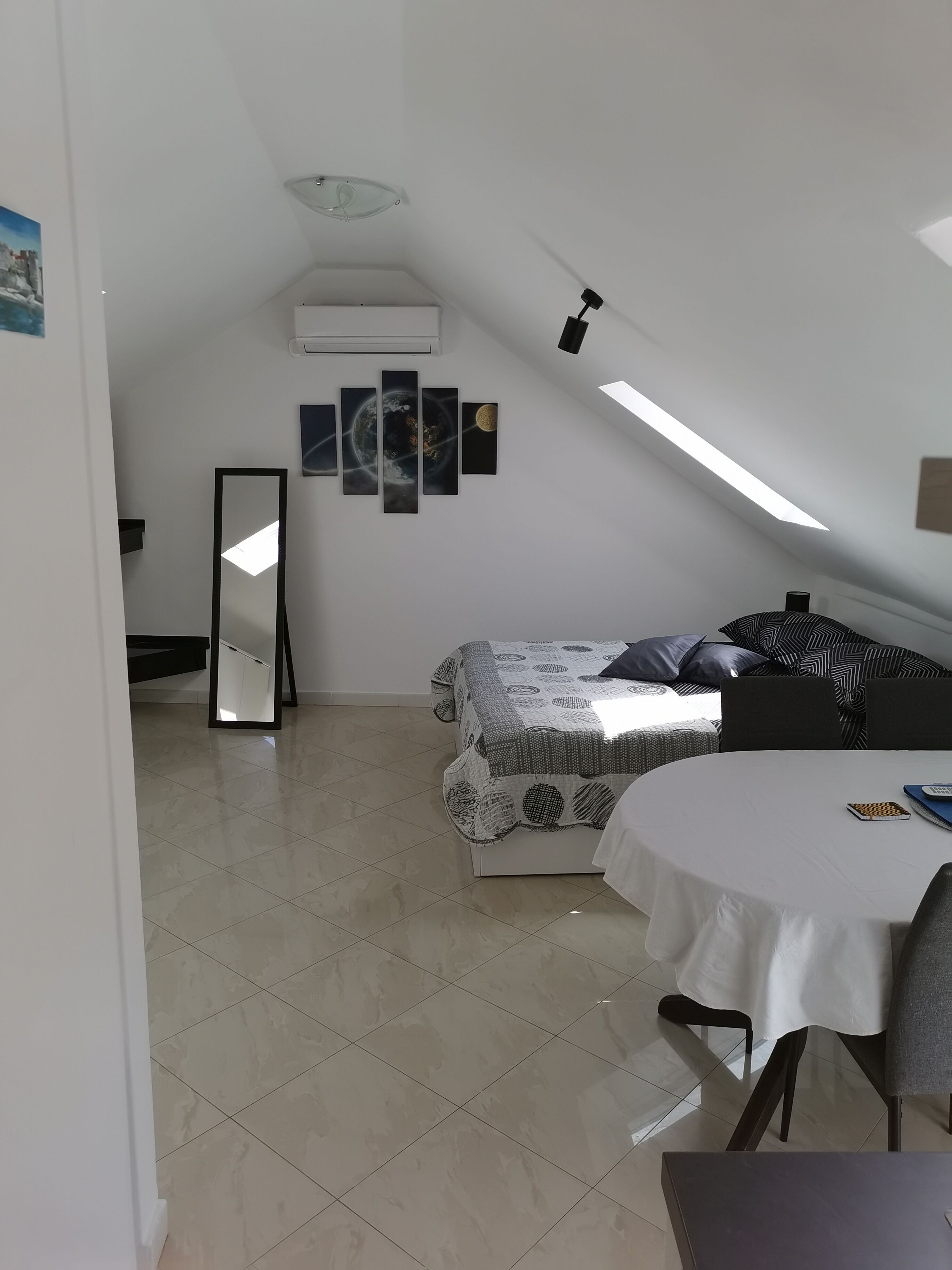 Un dormitorio con una cama, una mesa y una silla. Hay una lámpara en el techo, un aire acondicionado instalado en la pared y un cuadro enmarcado.