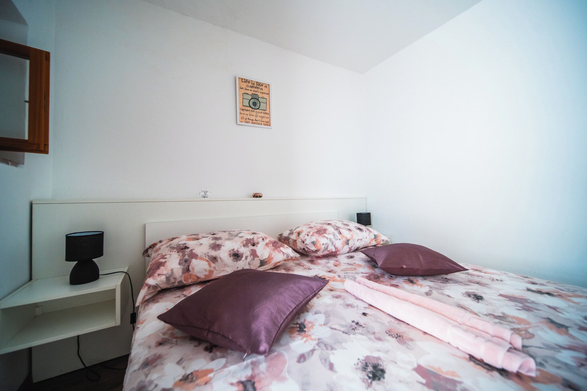 A bedroom with a bed, pillows, a nightstand, and a wall-mounted picture.
