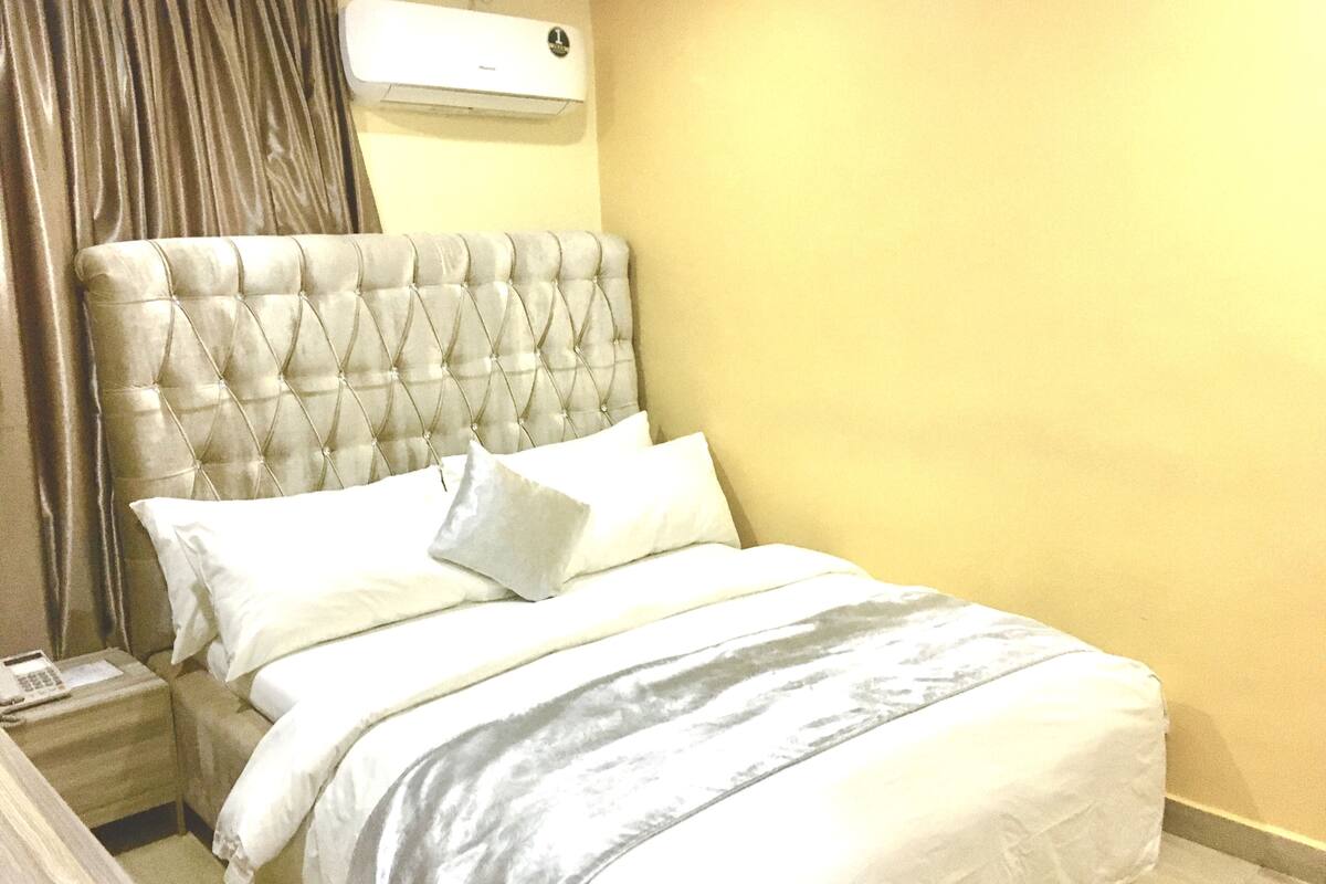 A neatly made bed with a tufted headboard, white bedding, and a bedside table with a lamp.