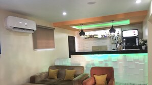 A modern living room with a sofa, armchair, and coffee table. A bar area with a counter and shelves of bottles is visible in the background. - Alexia's Place Hotel (Lagos)