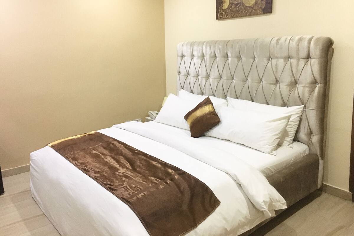 A neatly made bed with a tufted headboard, white and brown bedding, and a single decorative pillow.