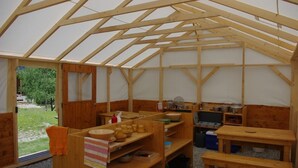 A rustic wooden structure with a high ceiling and a simple, functional interior. It includes wooden benches, tables, and shelves with various items. - Yourtes de Montagnes Insolites (Val-Cenis)