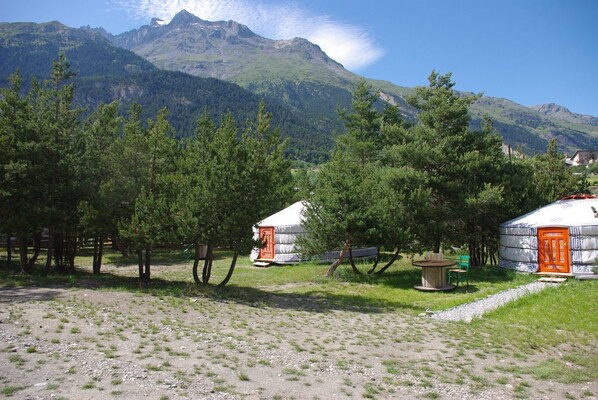 Yurts with orange doors, surrounded by trees, in a grassy area with mountains in the background. - Yourtes de Montagnes Insolites (Val-Cenis)