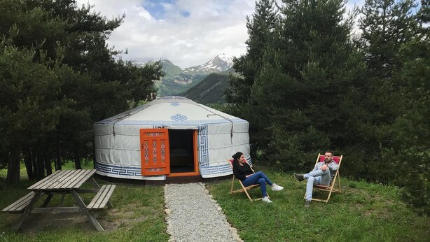 A yurt with an open door, a picnic table, and two people sitting on chairs outside. - Yourtes de Montagnes Insolites (Val-Cenis)