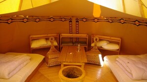 A cozy tent with two beds, a central table, and a small stool. - Yourtes de Montagnes Insolites (Val-Cenis)