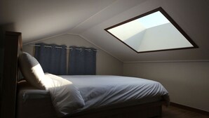 A bedroom with a skylight, a bed, and a window with curtains. - Daisy (Jeju City)
